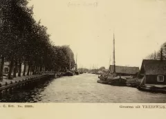 Gezicht op de Vaartsche Rijn te Vreeswijk uit het zuiden; met links een rij loofbomen langs de Dorpsstraat en rechts een vrachtschip en enkele loodsen.